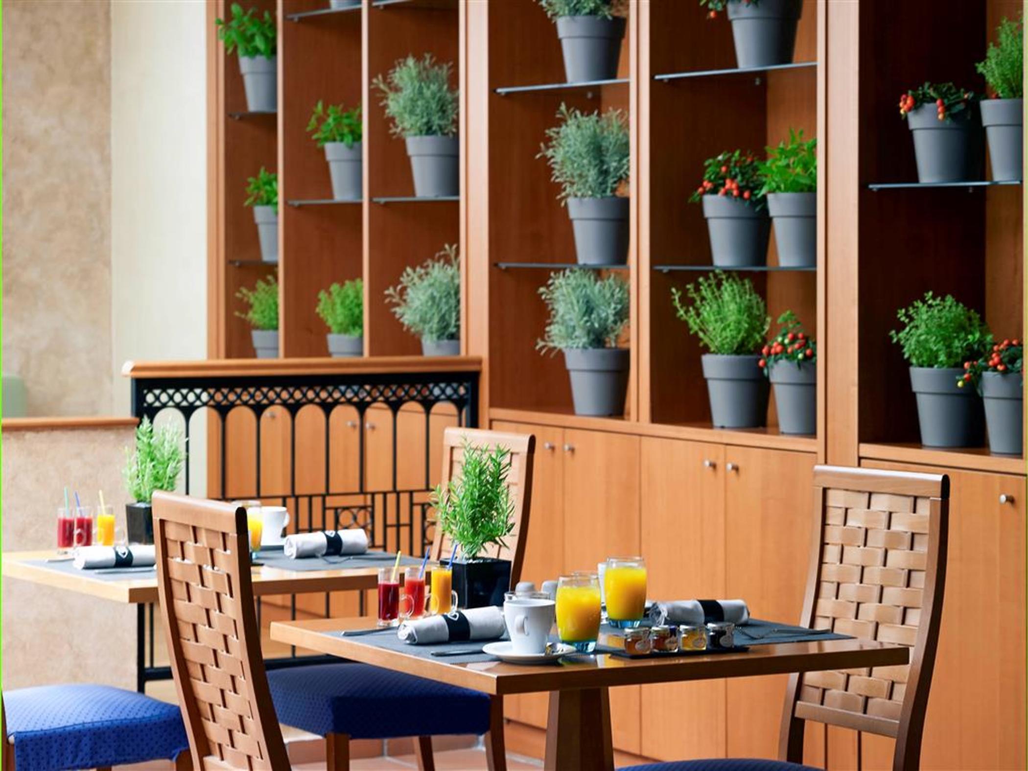 فندق سوفيتِل أثينا إيربورت Spáta المظهر الخارجي الصورة The photo depicts a cozy dining area, likely in a restaurant or hotel. There are wooden tables set with breakfast items, including glasses of fresh juice and other small dishes. The seating includes chairs with simple designs. Behind the tables, ther