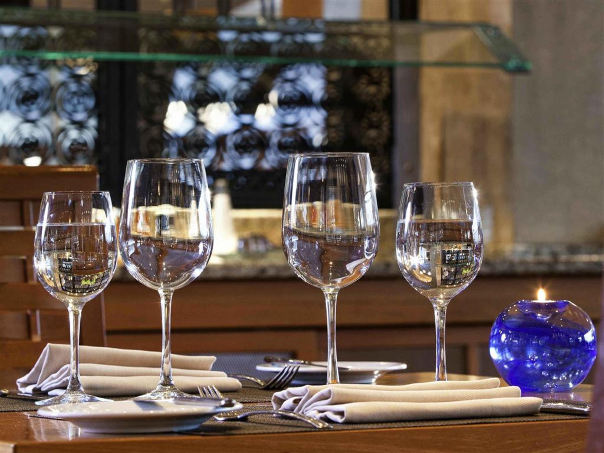 فندق سوفيتِل أثينا إيربورت Spáta المظهر الخارجي الصورة The photo shows a dining table set with four elegant wine glasses filled with water. The glasses are positioned in a row on the table. Next to each glass, there are neatly folded napkins and forks. There is also a small blue decorative candle holder 