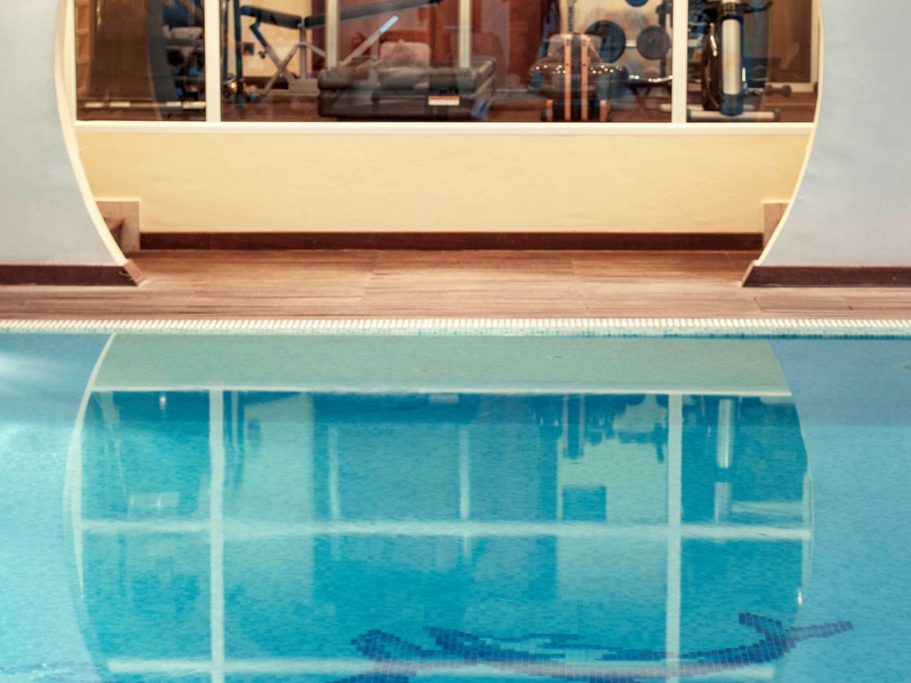 فندق سوفيتِل أثينا إيربورت Spáta المظهر الخارجي الصورة The image shows a swimming pool with a clear, blue surface reflecting the surrounding area. In the background, there appears to be a gym or fitness area visible through large windows. The pool has a tiled edge and features a design or pattern visible