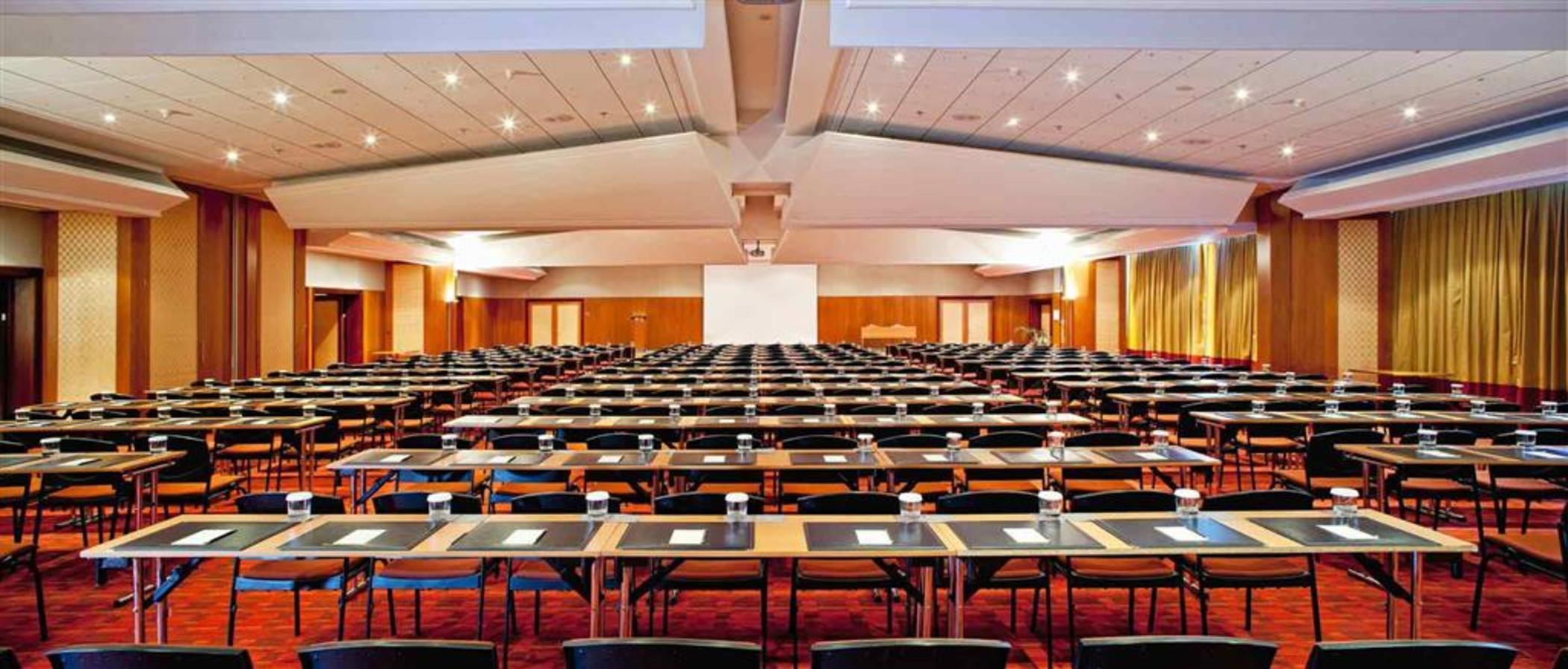 فندق سوفيتِل أثينا إيربورت Spáta المظهر الخارجي الصورة The photo shows a large conference room setup. The room is arranged with numerous tables organized in rows, facing a central presentation area. Each table has a notepad and a glass of water. There is a large blank white screen positioned at the front