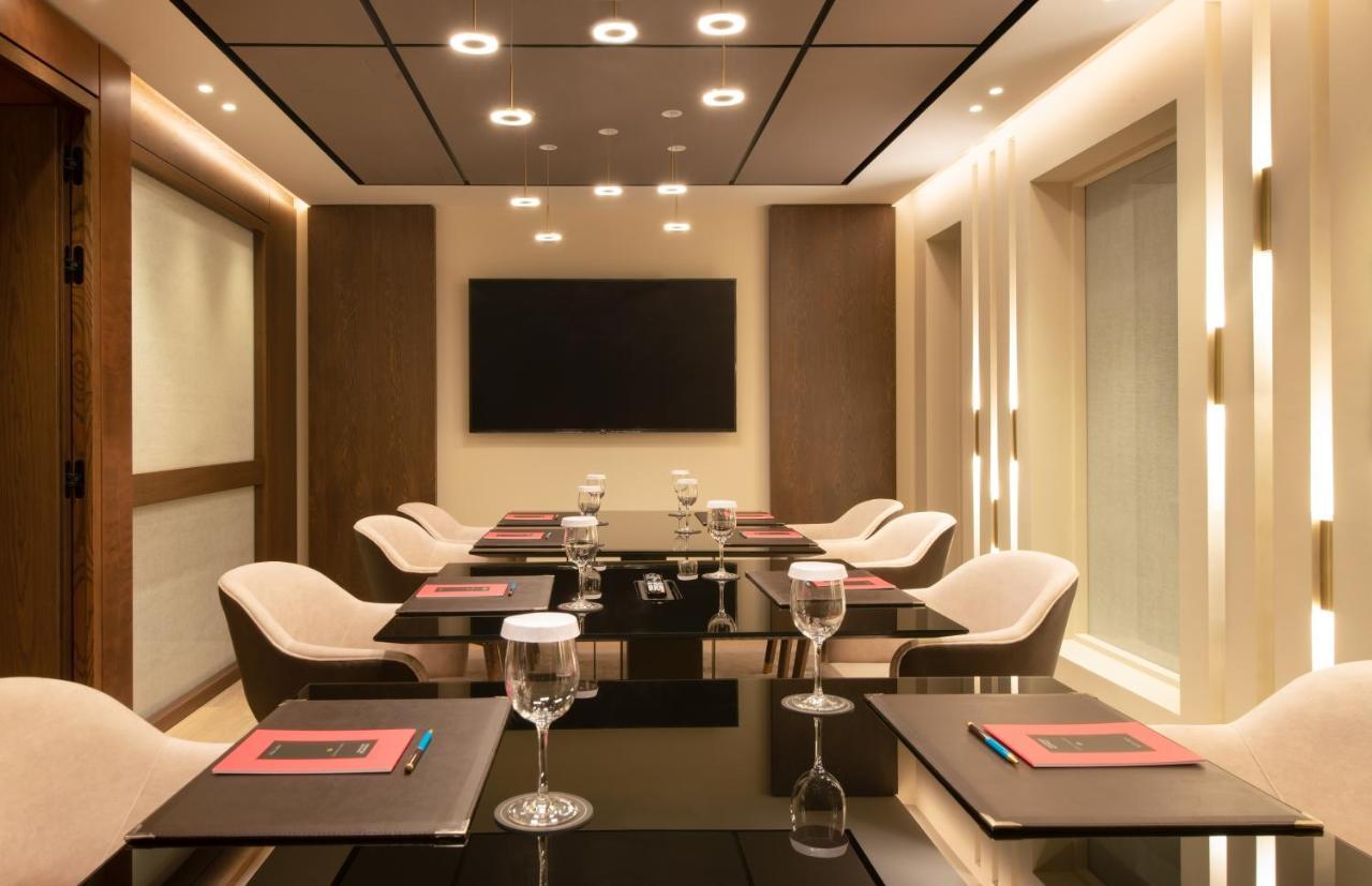 فندق سوفيتِل أثينا إيربورت Spáta المظهر الخارجي الصورة The photo depicts a modern conference room. It features a sleek glass table surrounded by stylish chairs. Each place setting includes a glass of water and a menu or notepad. The room is well-lit with recessed lighting and has a large flat-screen tele