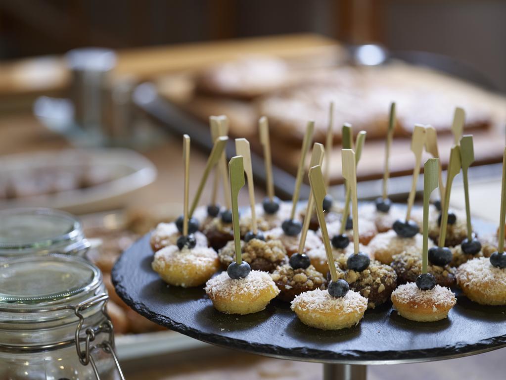 فندق سوفيتِل أثينا إيربورت Spáta المظهر الخارجي الصورة The photo displays a dessert selection featuring small pastries arranged on a slate serving platter. The pastries are topped with coconut and have a single blue berry on each, with decorative sticks inserted for easy handling. In the background, ther